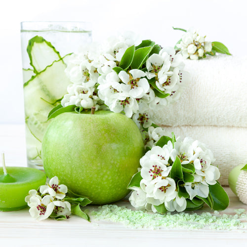 Wees Verrukkelijk Waxmelt – geurblokje van sojawas met groene appel, bessen, bloemen en lichte houtsoorten. Foto van groene appel met witte bloesems en frisse spa-styling.